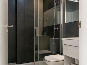 A modern bathroom with a glass-enclosed shower, a white toilet, and a dark tiled wall.
