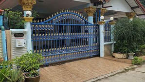 A gated entrance with a blue ornate gate, potted plants, and a tiled walkway leading to a building with a red-tiled roof. - Room in Guest Room - Stunning Home Great Location (Pattaya)