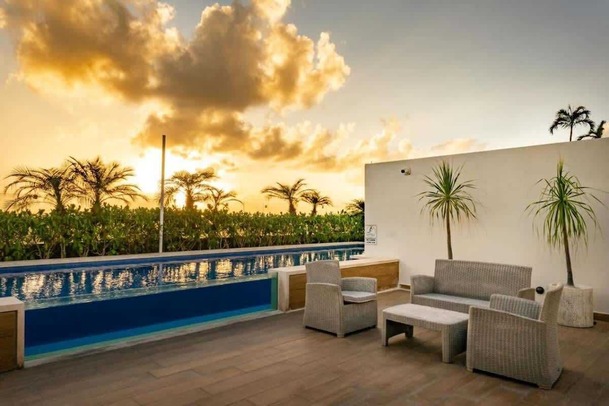 A rooftop pool area with a seating arrangement and a view of palm trees and a sunset.