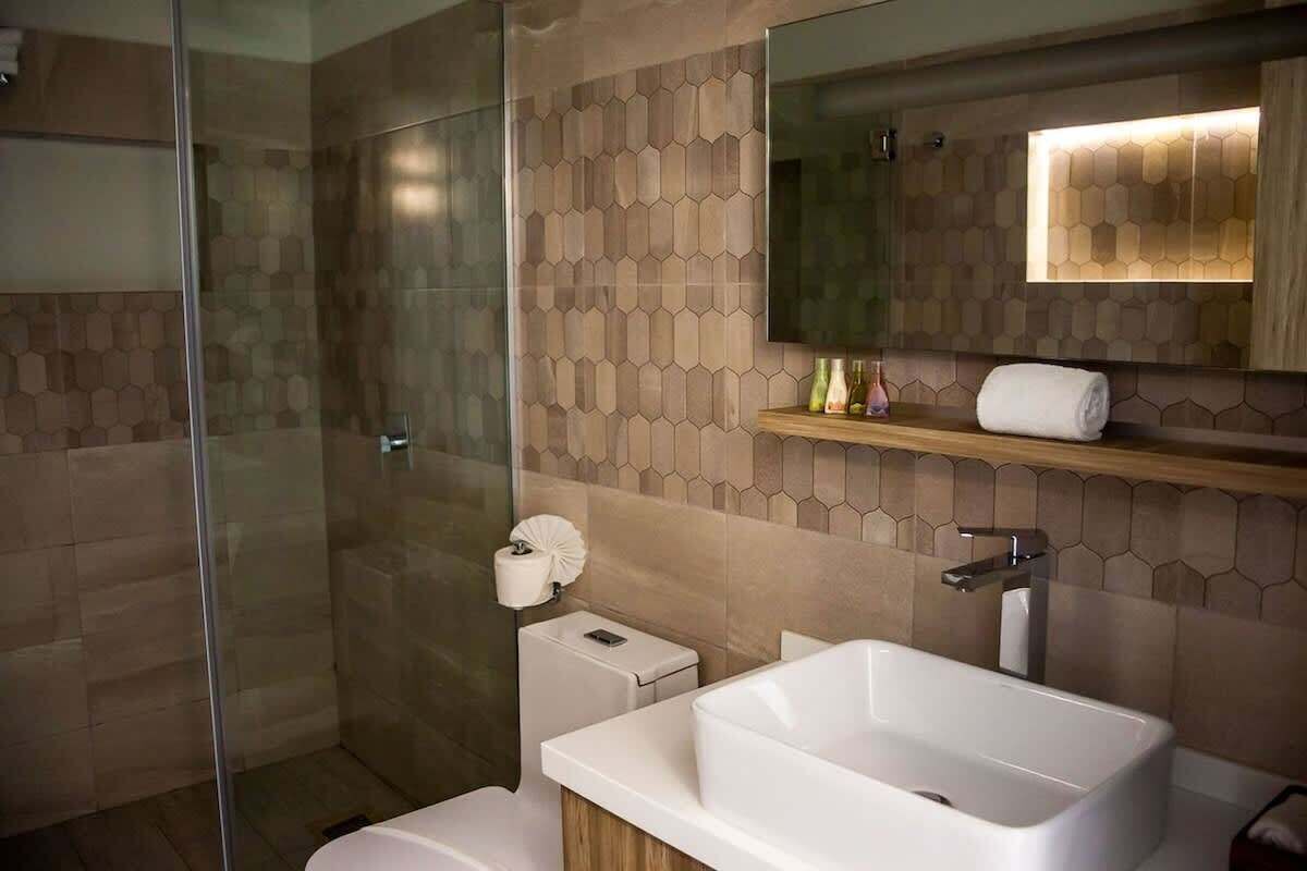 Un baño moderno con cabina de ducha de vidrio, un lavamanos amplio y un espejo sobre él.