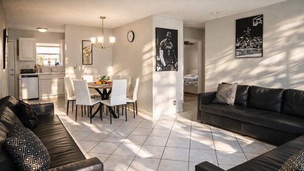 Ein modernes Wohnzimmer mit einem dunkelbraunen Ledersofa, einem Essbereich mit rundem Tisch und Stühlen sowie einer Küche im Hintergrund.