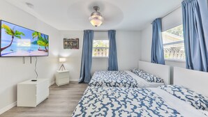 Ein Schlafzimmer mit zwei Betten, einem Wandfernseher, einem Deckenventilator und einem Fenster mit Vorhängen.
