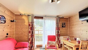 Una habitación acogedora con detalles de madera, un sofá rojo, una mesa de comedor con sillas y un televisor instalado en la pared.