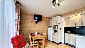 Un espacio habitable compacto con comedor, kitchenette y televisor de pantalla plana montado en la pared.