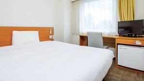 Ένα δωμάτιο ξενοδοχείου με ένα μεγάλο κρεβάτι, ένα γραφείο με υπολογιστή, μια τηλεόραση και ένα μικρό ψυγείο.