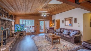 A spacious living room with a wooden ceiling, a large TV, a fireplace, and a cozy seating area with a leather couch and a coffee table. - Byrd Mountain - Upper Canyon Gem - Large Game Room (Ruidoso)