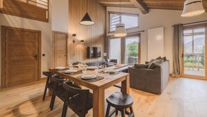 A spacious living area with a wooden dining table set for four, a gray sofa, and a television mounted on the wall. - Wifi, swimming pool, sauna, hammam, terrace, balcony, parking, tv, ski locker, 77m², Megève (Megève)