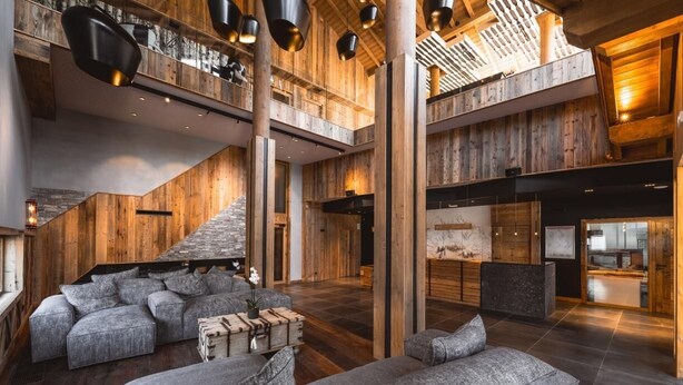 Een ruime lobby met een hoge plafond, houten details en moderne meubels.