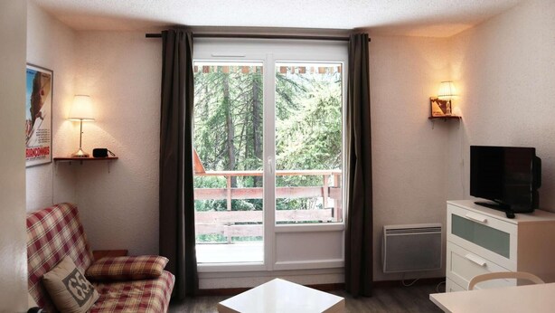 A room with a plaid sofa, a small table, a TV on a cabinet, and a window with curtains. - 10m from ski slopes, 2nd floor, balcony, ski locker, 24m², Les Orres (Les Orres)