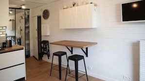 Een moderne keuken met een houten aanrecht, twee zwarte krukken, een witte kast en een aan de muur bevestigde televisie.