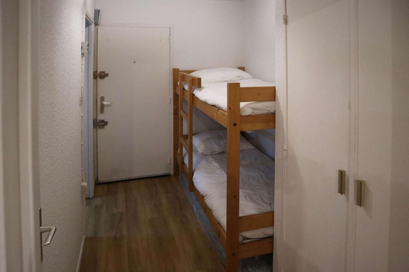 Un pasillo estrecho con una litera de madera y una puerta.