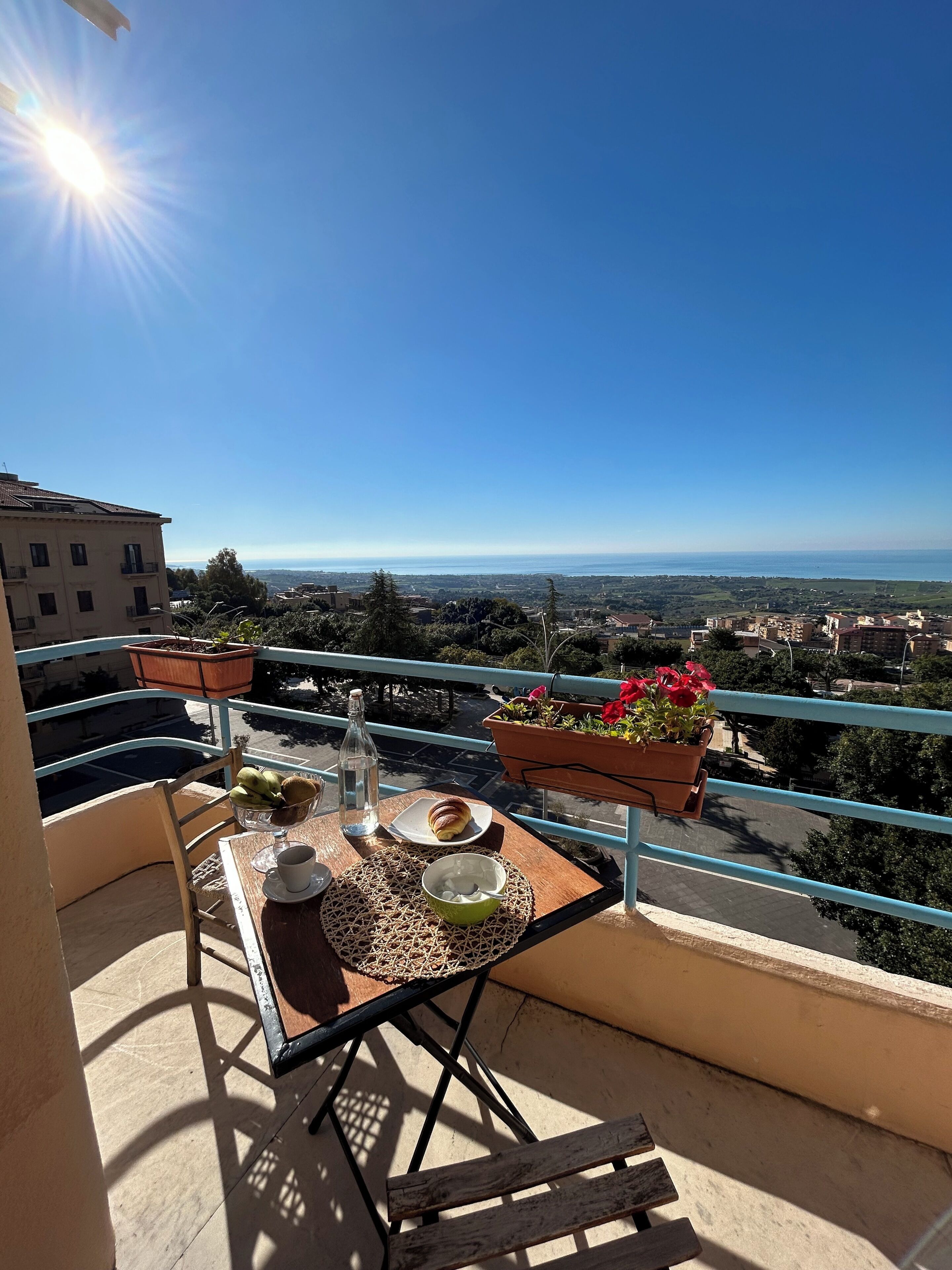 Ein Balkon mit Tisch für zwei Personen, Blumentöpfen und Blick auf die Stadt.
