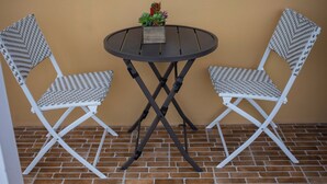 Two white wicker chairs with a small table in between, placed on a brick floor against a beige wall with a window above. - Modern Comfort: Private 1BR In Basseterre (Basseterre)