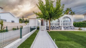 A modern house with a white facade, a patterned walkway, and a tree in the center.