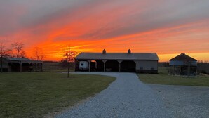 A gravel driveway leading to a barn with multiple open doors, surrounded by grassy fields and a sunset sky. - Cozy building in charming Loretto with WiFi, AC (Loretto)