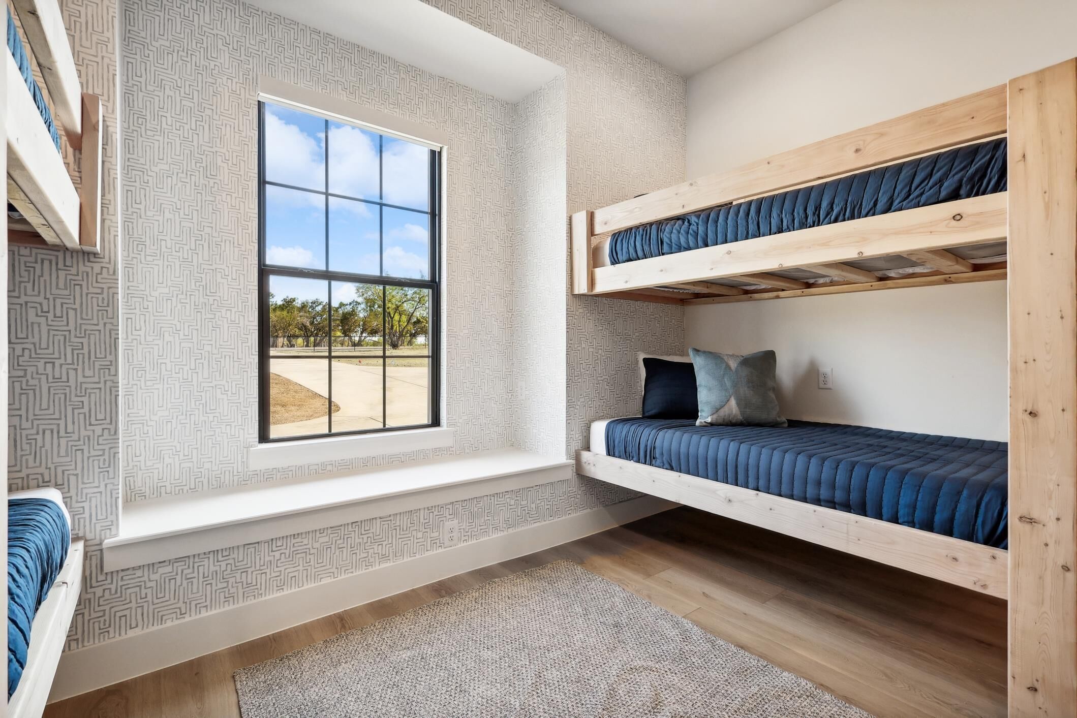 A room with bunk beds, a large window, and patterned wallpaper.
