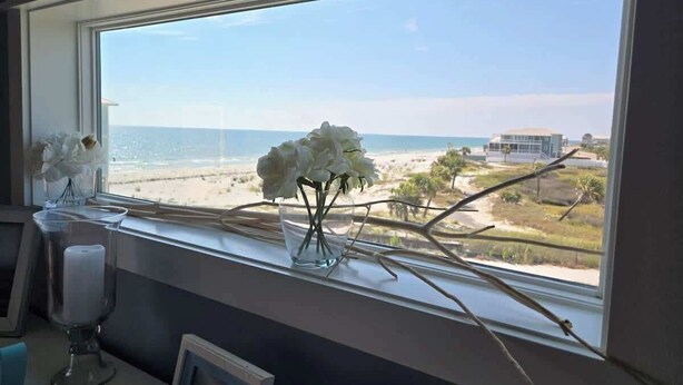 A window with a view of the beach and ocean, a vase with white flowers, and a candle holder. - Cape Ocean Front~Jacuzzi~Elevator~Arcade Games! (Port St. Joe)