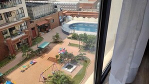 A courtyard with a pool, palm trees, and playground equipment. - Lenayan Park View Deluxe Double Room (Nairobi)