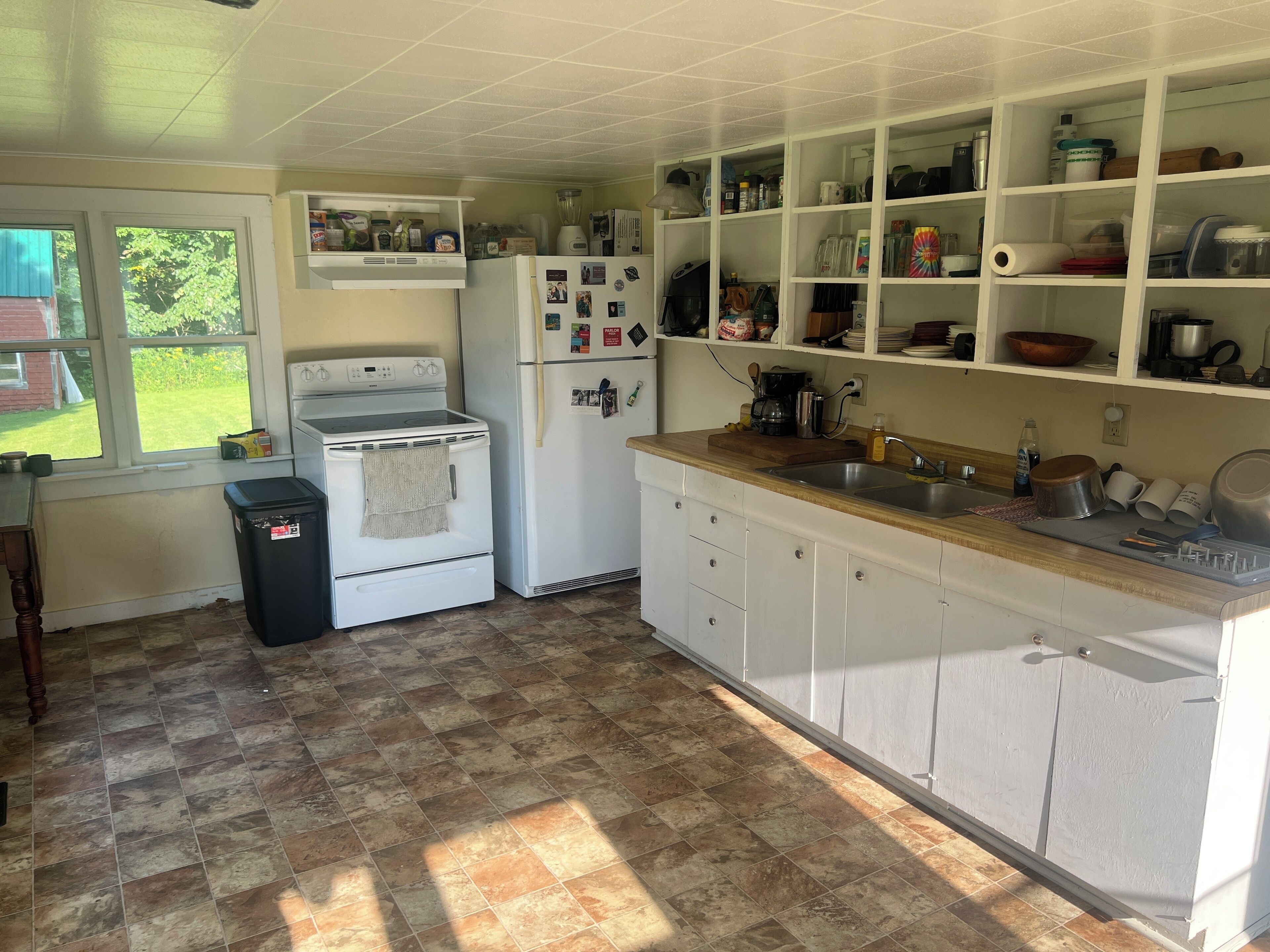 A kitchen with a stove, oven, refrigerator, and a sink. There is a window with a view of greenery outside.