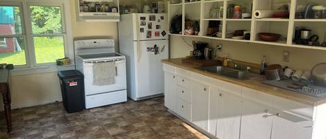 A kitchen with a stove, oven, refrigerator, and a sink. There is a window with a view of greenery outside.