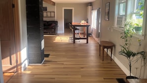 A spacious living area with a wooden floor, a dining table with chairs, a black leather sofa, and a potted plant.
