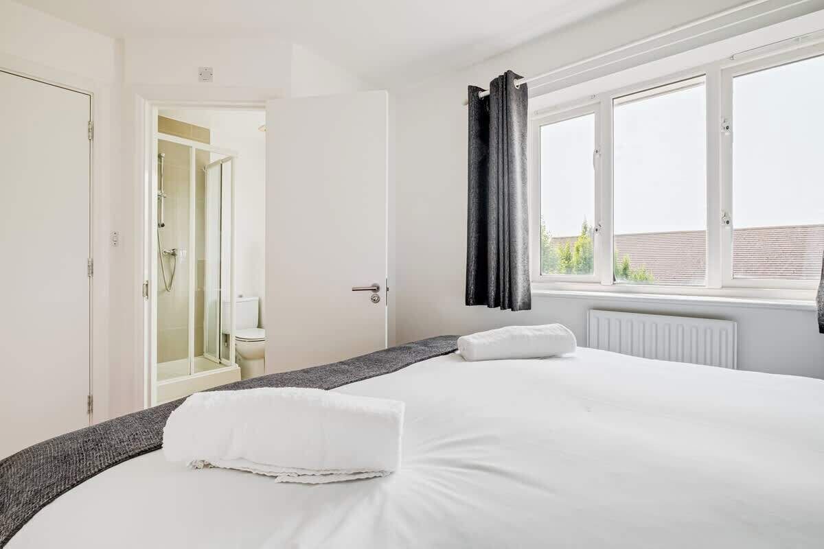 Habitación de hotel con cama, ventana con cortinas, radiador y puerta que da a un baño.