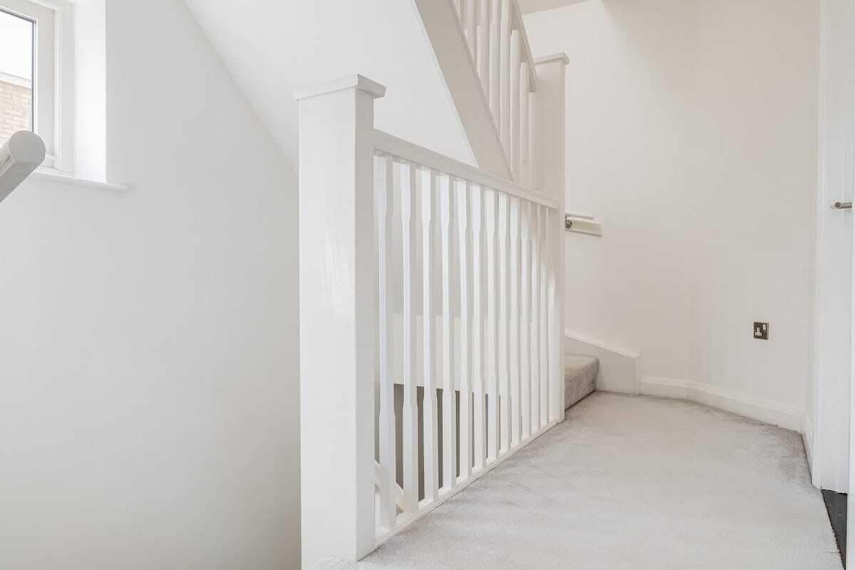 Un pasillo interior blanco con barandilla blanca, suelo alfombrado y una puerta a la derecha.