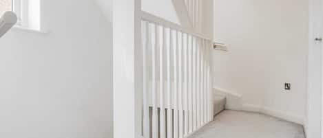 Un pasillo interior blanco con barandilla blanca, suelo alfombrado y una puerta a la derecha.