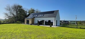Une maison moderne dotée d’un toit en pente, de grandes fenêtres et de panneaux solaires.