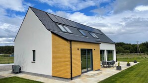A modern house with a sloped roof, large windows, and a patio area with outdoor furniture. - Ash Mill - Dornoch (Dornoch)