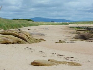 Une plage de sable parsemée de rochers et bordée d’une zone herbeuse.