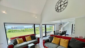 A spacious living area with two red and grey sofas, a grey rug, and a large window offering a view of a garden and buildings. - Ash Mill - Dornoch (Dornoch)