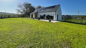 A modern house with a large lawn, solar panels, and a clear blue sky. - Ash Mill - Dornoch (Dornoch)