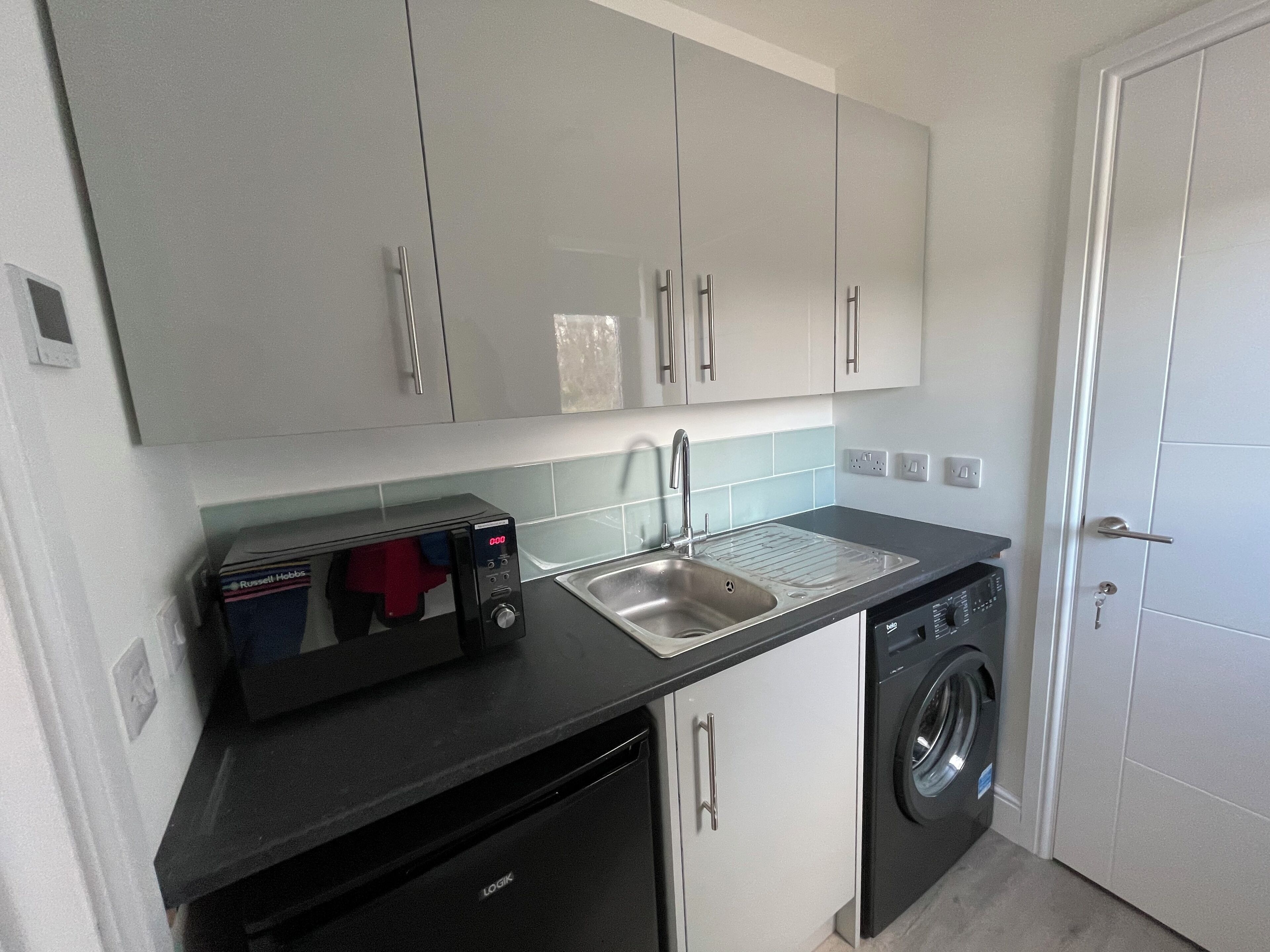 Een kleine keuken met een magnetron, spoelbak en wasmachine.