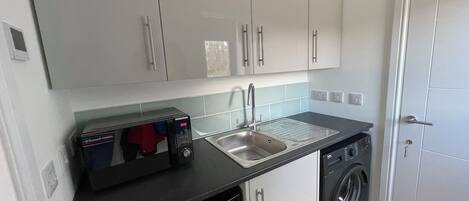 Een kleine keuken met een magnetron, spoelbak en wasmachine.
