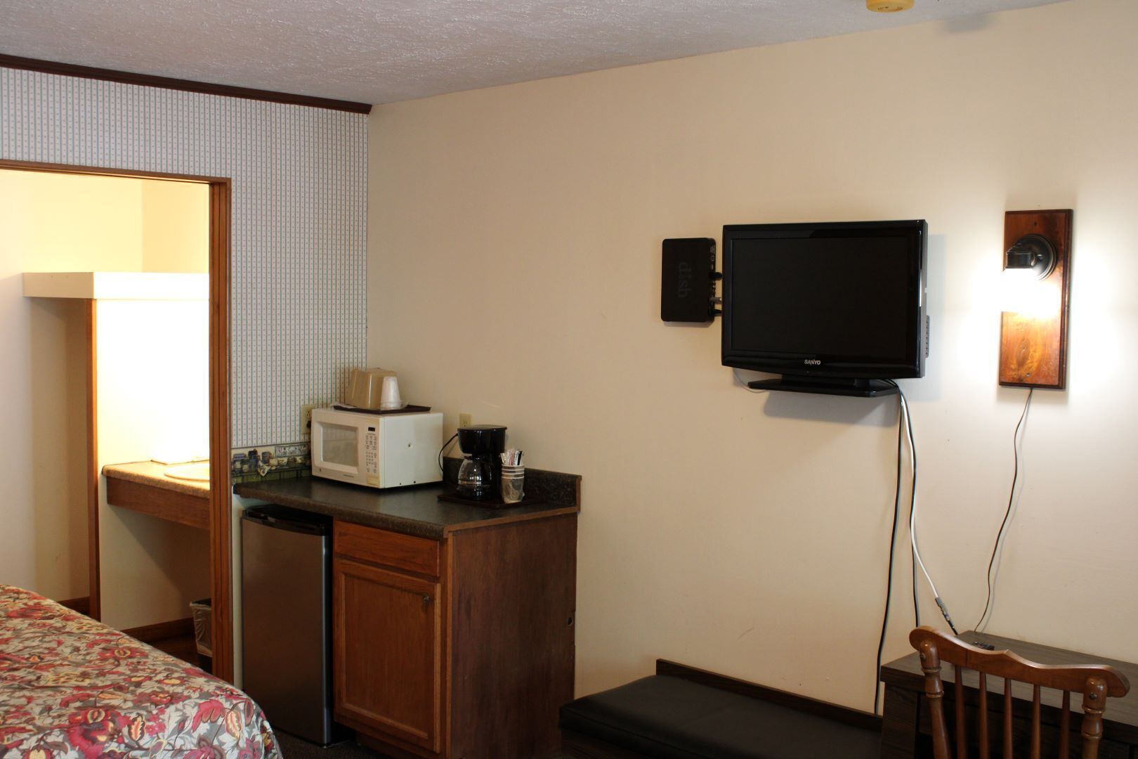 Ein Hotelzimmer mit einem Bett, einem Schreibtisch mit Mikrowelle, einer Kaffeemaschine, einem Fernseher und einem kleinen Holzstuhl.