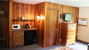 A compact room with wooden paneling, a microwave, a coffee maker, a small refrigerator, a television, and a dresser. - Two Rivers Lodge (Bryson City)
