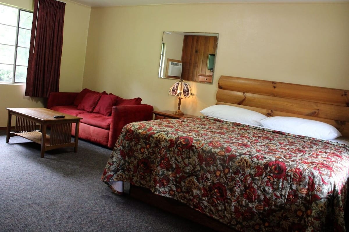 Un dormitorio con cama de cabecera de madera, un sofá rojo, una mesa de madera y un espejo en la pared.