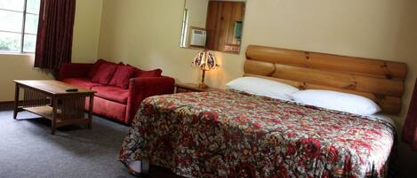 A bedroom with a wooden headboard bed, a red sofa, a wooden table, and a mirror on the wall.