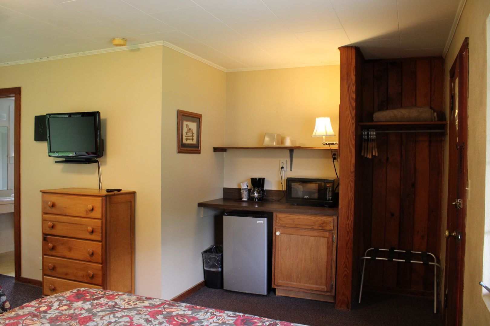 A compact room with a bed, a small kitchenette, a television, and a wooden wardrobe.