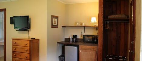 A compact room with a bed, a small kitchenette, a television, and a wooden wardrobe.