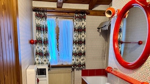A compact bathroom with a toilet, bidet, and sink. There is a window with patterned curtains, a radiator, and a red wall-mounted mirror. - Appartamento Marele (Folgarida)