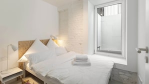 Une chambre à coucher avec un lit, une table de chevet avec une lampe, une fenêtre donnant sur un beau paysage et un mur en pierre.