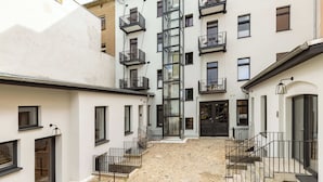 Une cour dallée de pierres, un escalier central et de nombreux balcons aménagés avec du mobilier d’extérieur.