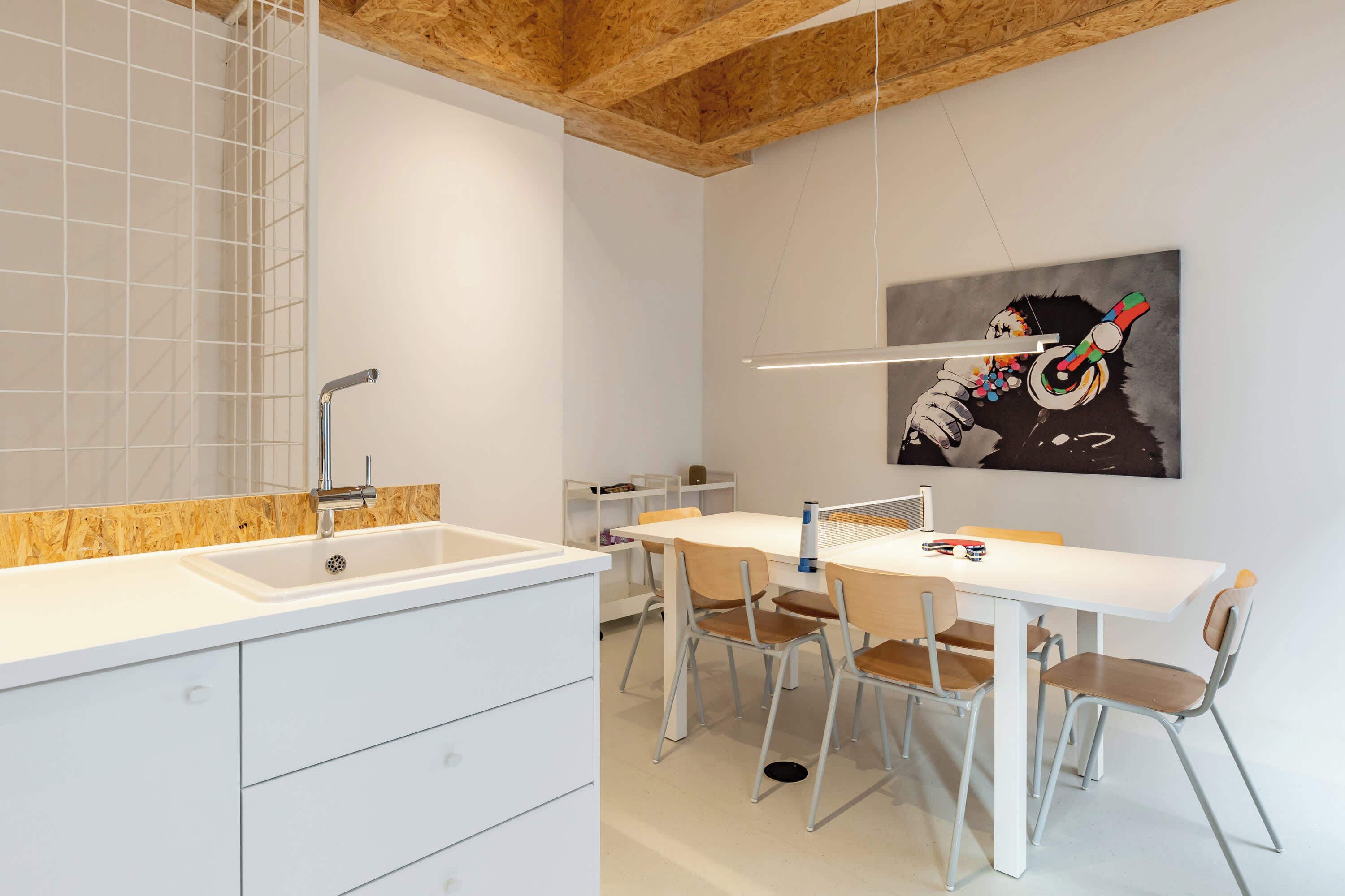 Een moderne keuken met witte kasten, een houten plafond en een eethoek met een witte tafel en stoelen.