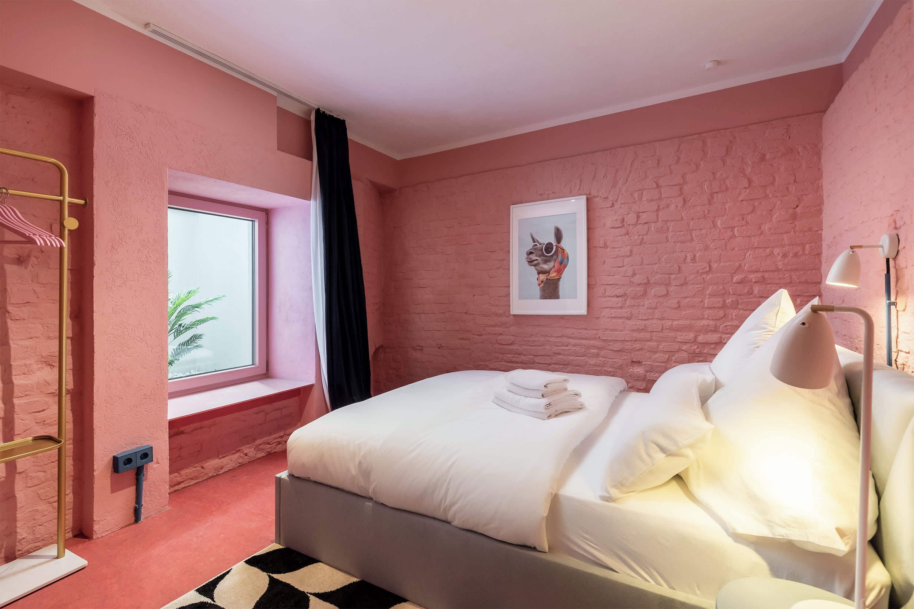 Ein Schlafzimmer mit rosafarbenen Ziegelwänden, einem Bett, einem Fenster, einem gerahmten Bild und einer Lampe.