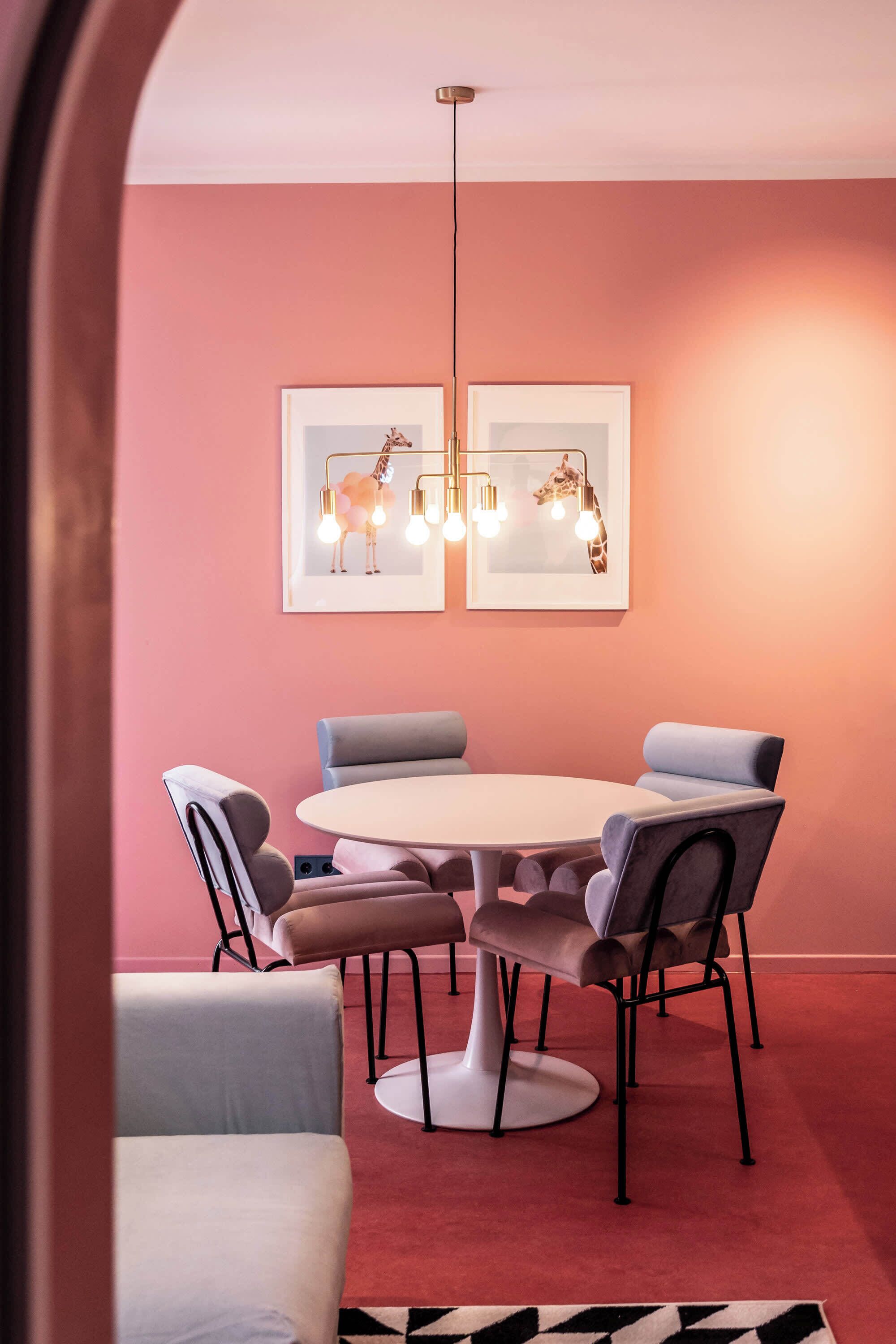 Ein Essbereich mit einem runden Tisch, sechs Stühlen, einer rosa Wand und zwei Bildern über dem Tisch.