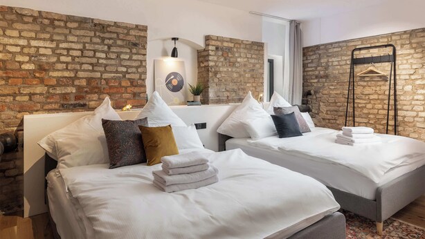 A hotel room with two beds, white linens, a brick wall, a mirror, and a hanging coat rack. - Industrial Loft Duplex (100sqm) near Antonplatz (Berlin)