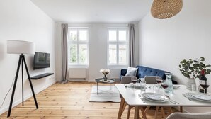 Een moderne woonkamer met een bank, een eettafel en een aan de muur bevestigde televisie.