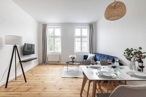 A modern living room with a sofa, dining table, and a TV mounted on the wall.